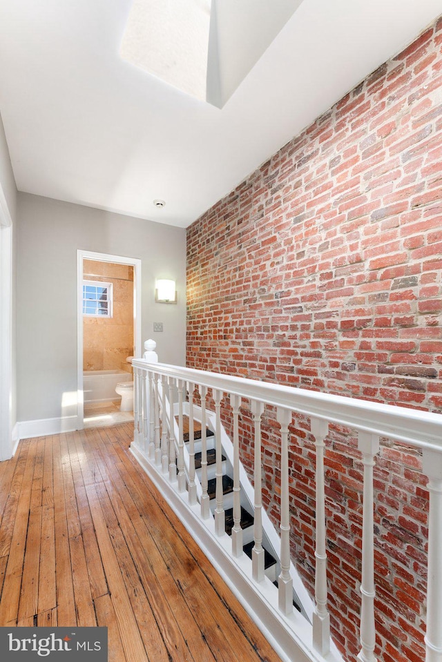 hallway featuring hardwood / wood-style floors, an upstairs landing, baseboards, and brick wall