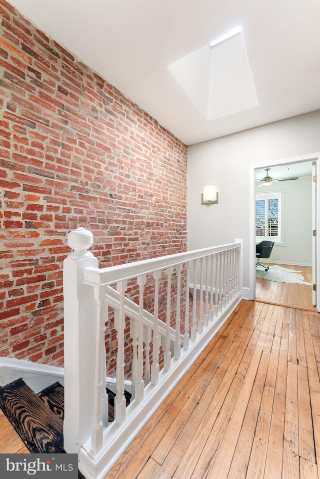 hallway featuring hardwood / wood-style flooring, a skylight, an upstairs landing, and brick wall