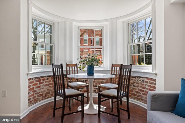 dining room featuring plenty of natural light, wood finished floors, and brick wall