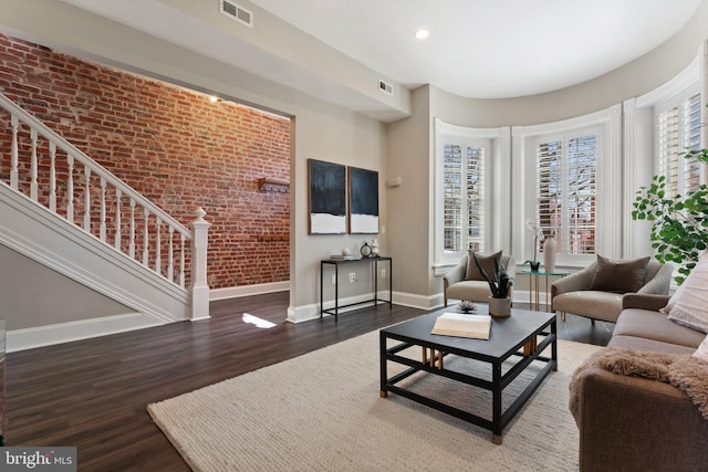 living area featuring visible vents, brick wall, baseboards, stairway, and wood finished floors