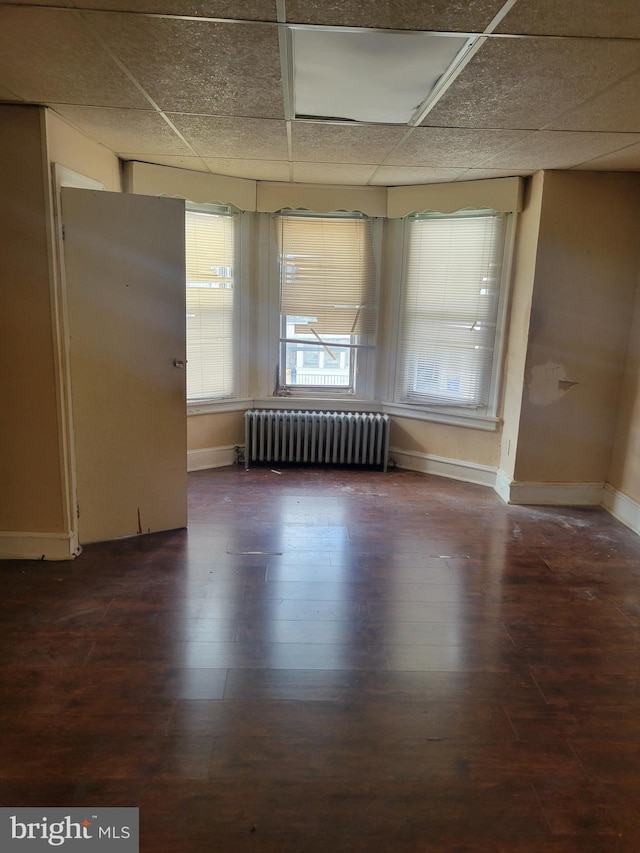 unfurnished room featuring radiator, wood finished floors, baseboards, and a drop ceiling