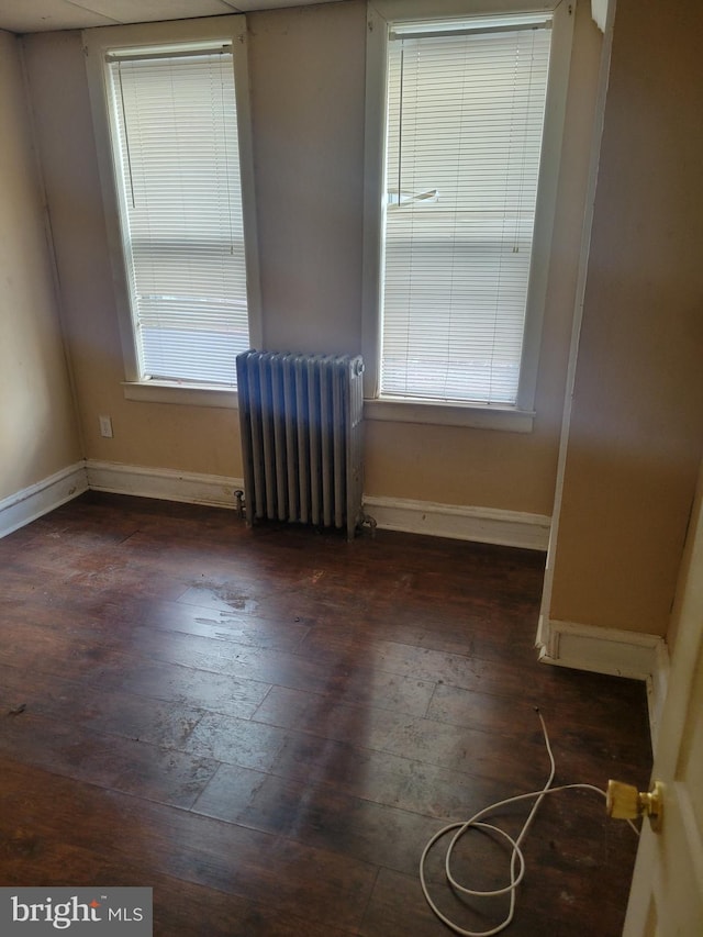 empty room featuring baseboards, radiator, and dark wood-style floors