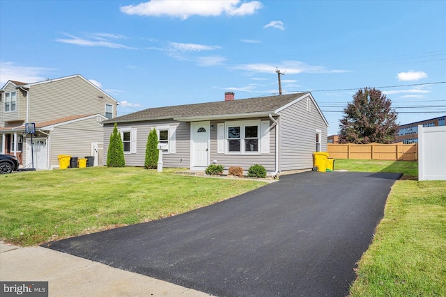 view of front facade with driveway, fence, a front yard, a shingled roof, and a chimney