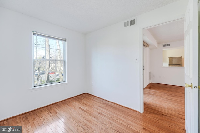 spare room featuring visible vents, wood-type flooring, and a healthy amount of sunlight