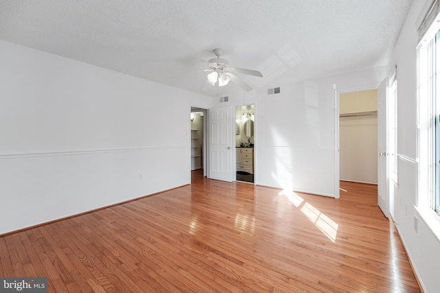 unfurnished bedroom with a walk in closet, light wood-style floors, visible vents, and a textured ceiling