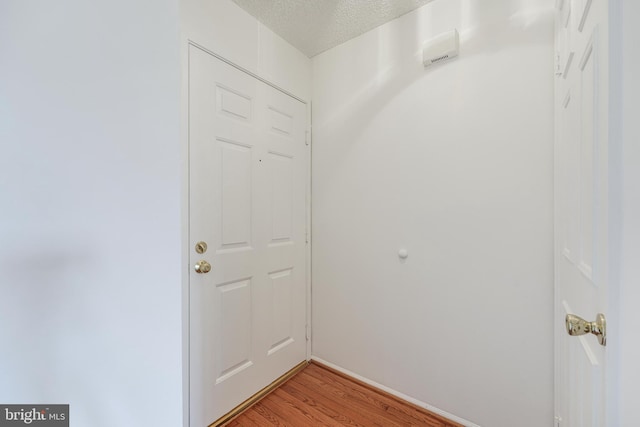 corridor with baseboards, light wood finished floors, and a textured ceiling