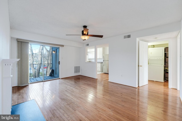 unfurnished living room with light wood-type flooring, stacked washer / drying machine, and visible vents