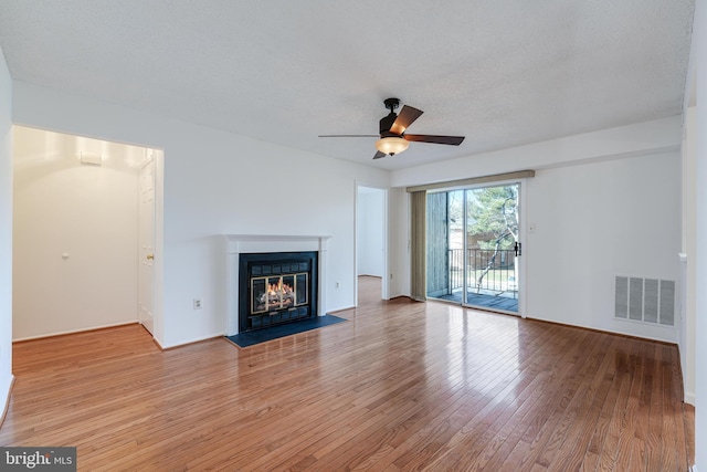 unfurnished living room featuring visible vents, light wood-type flooring, a glass covered fireplace, a textured ceiling, and a ceiling fan