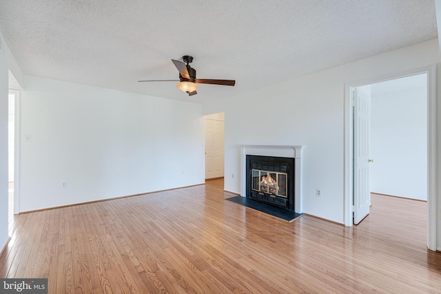 unfurnished living room featuring light wood finished floors, baseboards, ceiling fan, a fireplace with flush hearth, and a textured ceiling