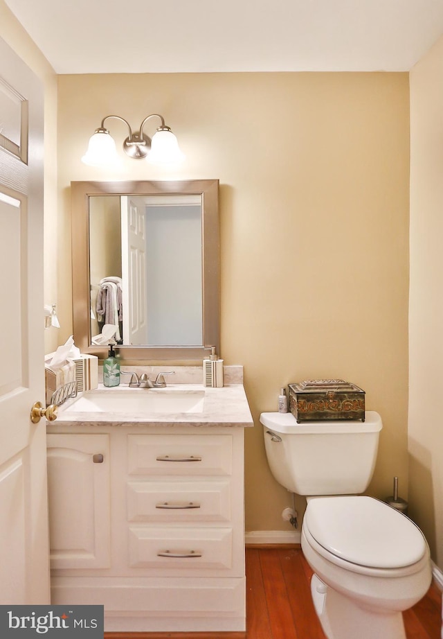 half bathroom with baseboards, toilet, wood finished floors, and vanity