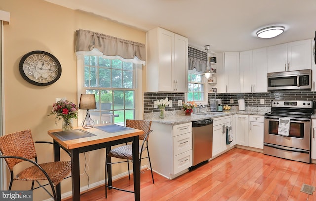 kitchen with white cabinets, backsplash, light wood-style flooring, and appliances with stainless steel finishes