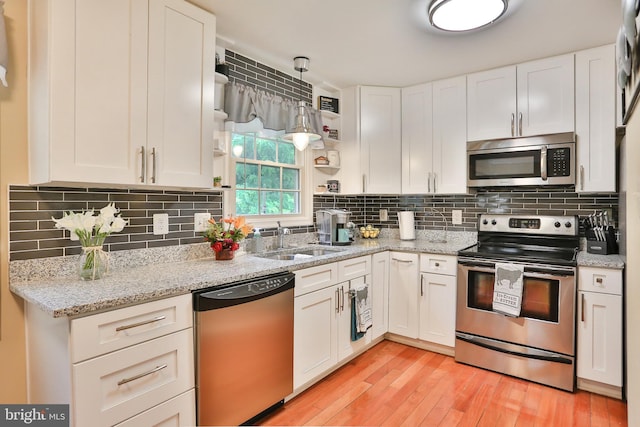 kitchen featuring light wood finished floors, decorative backsplash, stainless steel appliances, white cabinetry, and a sink