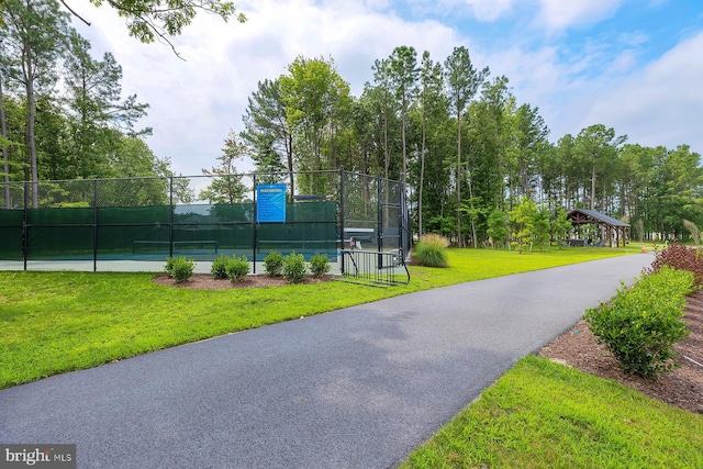 view of home's community featuring a tennis court, a yard, and fence