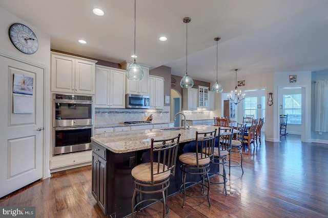 kitchen with an island with sink, a sink, tasteful backsplash, appliances with stainless steel finishes, and white cabinets