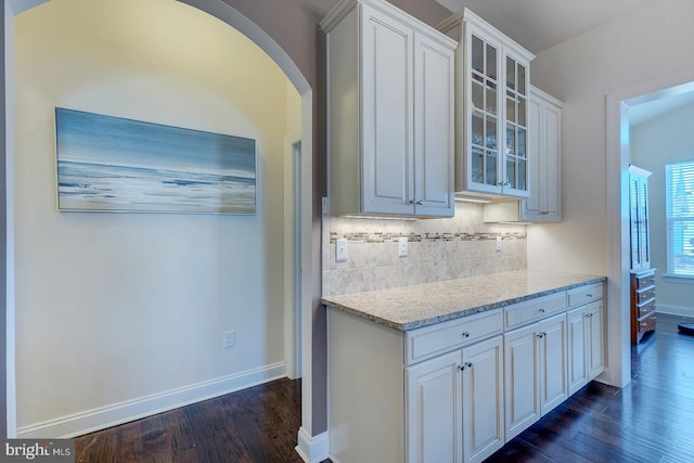 kitchen with backsplash, glass insert cabinets, dark wood-type flooring, baseboards, and arched walkways