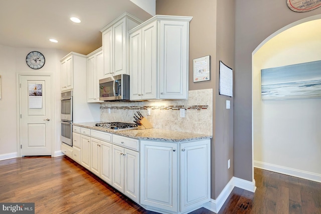 kitchen featuring dark wood-style floors, arched walkways, appliances with stainless steel finishes, white cabinetry, and backsplash