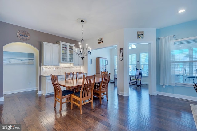 dining space featuring arched walkways, baseboards, an inviting chandelier, and dark wood-style flooring