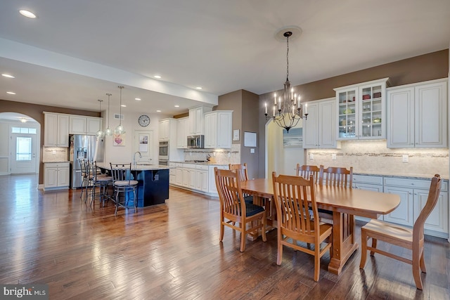 dining room featuring arched walkways, a chandelier, recessed lighting, and dark wood-style floors