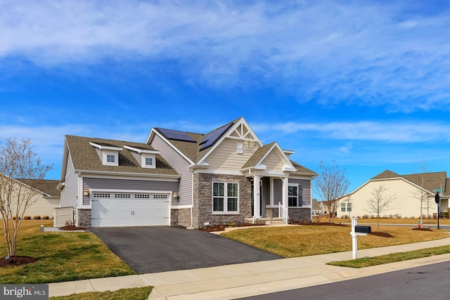 craftsman-style house with driveway, stone siding, roof mounted solar panels, a front yard, and a garage