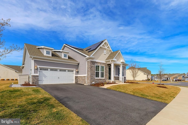 craftsman house featuring a front lawn, aphalt driveway, stone siding, roof mounted solar panels, and a garage