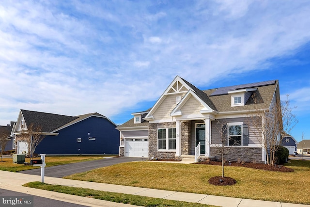 craftsman-style home with a front yard, stone siding, a garage, aphalt driveway, and roof mounted solar panels