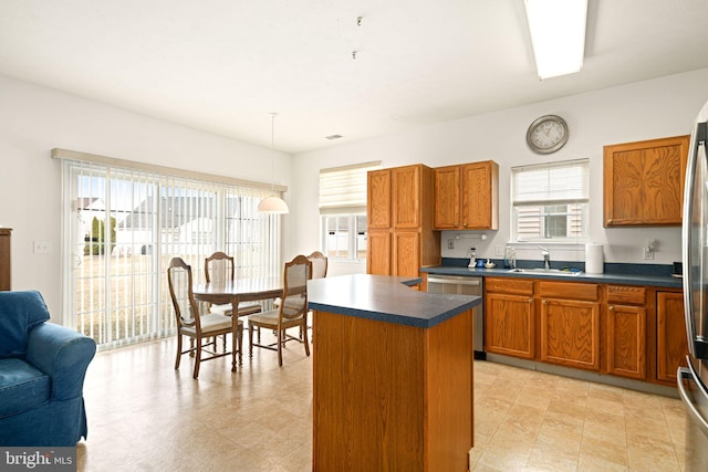 kitchen featuring stainless steel dishwasher, dark countertops, brown cabinetry, and a kitchen island