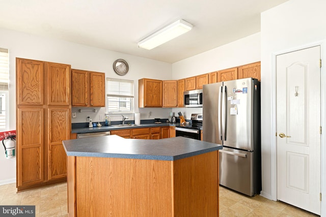 kitchen featuring brown cabinetry, a sink, stainless steel appliances, dark countertops, and a center island