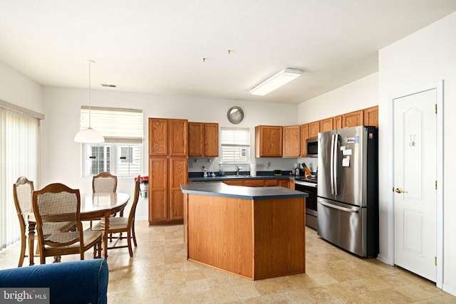 kitchen featuring dark countertops, a kitchen island, pendant lighting, brown cabinets, and appliances with stainless steel finishes