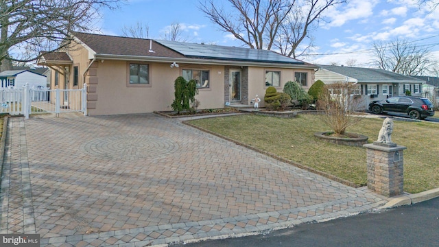 ranch-style house with fence, solar panels, stucco siding, a front lawn, and decorative driveway