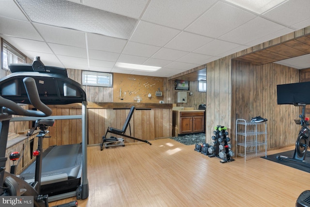 workout room featuring wooden walls, a drop ceiling, and wood finished floors