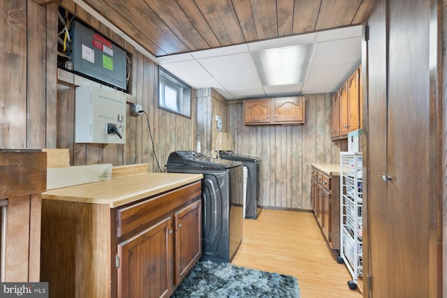 laundry room with light wood finished floors, independent washer and dryer, cabinet space, and wood walls