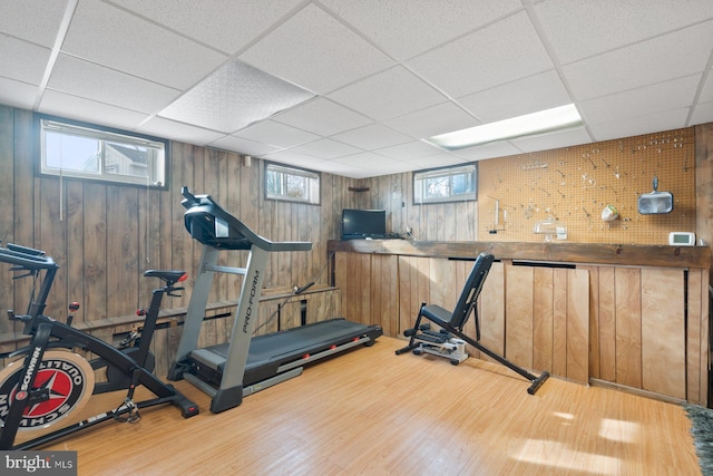 workout room featuring wood walls, a paneled ceiling, and wood finished floors