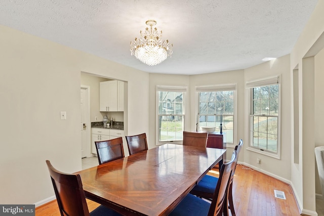 dining space featuring baseboards, visible vents, light wood finished floors, a textured ceiling, and a notable chandelier