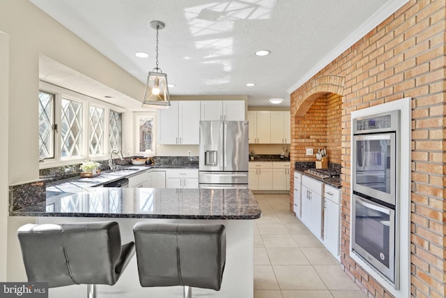 kitchen featuring a sink, appliances with stainless steel finishes, a peninsula, white cabinets, and light tile patterned floors