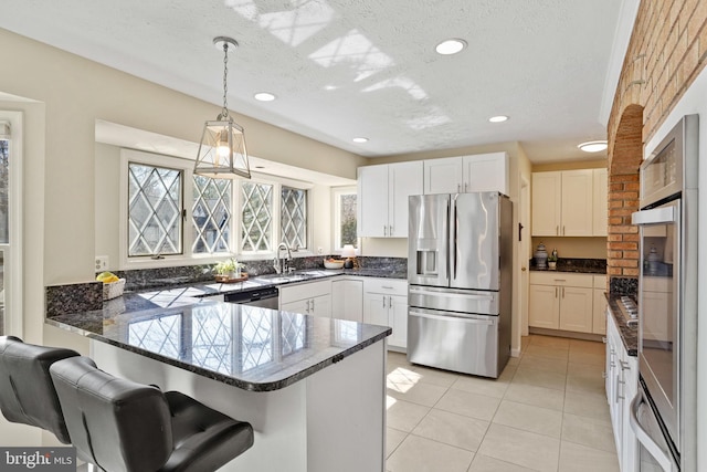 kitchen featuring dark stone countertops, appliances with stainless steel finishes, a peninsula, hanging light fixtures, and a sink