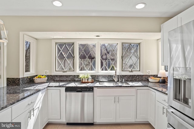 kitchen with a sink, dark stone countertops, white cabinetry, appliances with stainless steel finishes, and light tile patterned floors