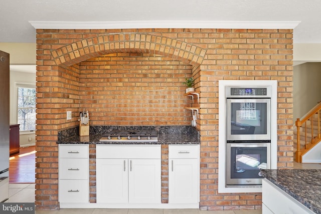 kitchen featuring light tile patterned floors, dark stone countertops, stainless steel appliances, a textured ceiling, and white cabinetry