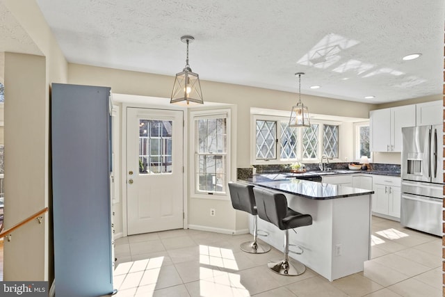 kitchen with dark countertops, light tile patterned floors, a peninsula, stainless steel refrigerator with ice dispenser, and white cabinetry