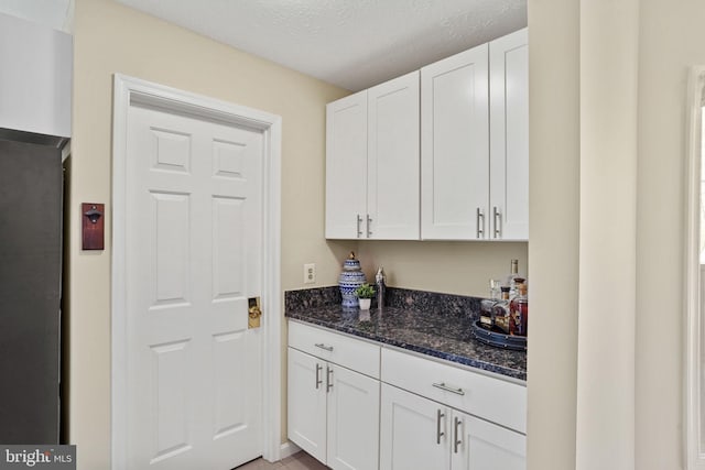 kitchen with dark stone countertops, a textured ceiling, and white cabinetry