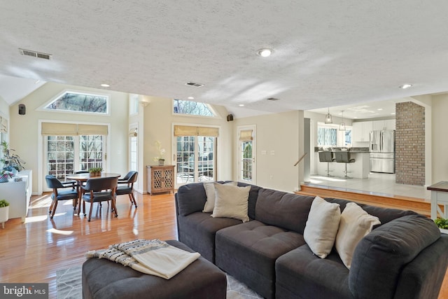 living area with lofted ceiling, a healthy amount of sunlight, visible vents, and light wood finished floors