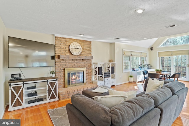 living room with wood finished floors, visible vents, vaulted ceiling, a textured ceiling, and a brick fireplace