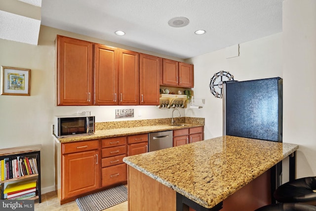 kitchen featuring light stone counters, a peninsula, stainless steel dishwasher, freestanding refrigerator, and a sink