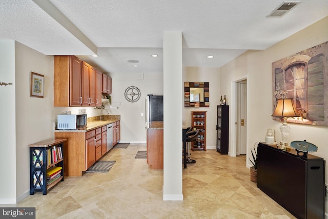 kitchen featuring light stone counters, brown cabinetry, visible vents, a sink, and dishwasher