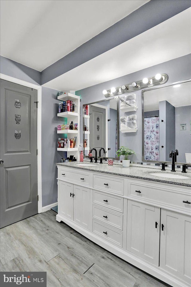 bathroom featuring double vanity, wood finished floors, baseboards, and a sink