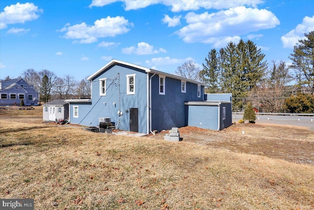 back of property featuring central AC unit, a lawn, and stucco siding