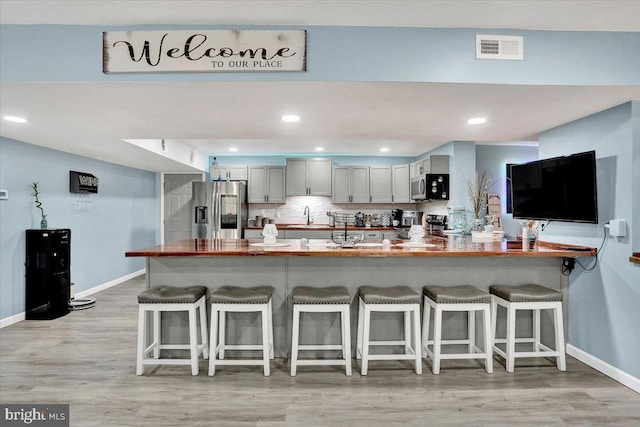 kitchen with visible vents, a peninsula, a sink, decorative backsplash, and appliances with stainless steel finishes