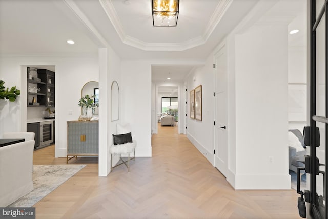 corridor with a tray ceiling, recessed lighting, wine cooler, crown molding, and baseboards