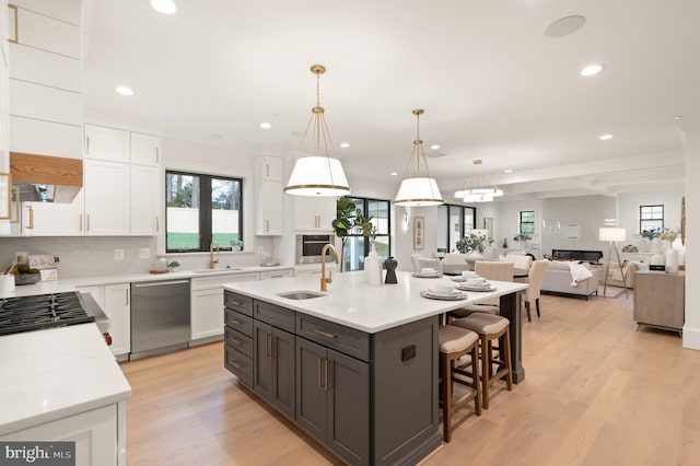 kitchen featuring a center island with sink, light wood-style flooring, a sink, stainless steel appliances, and white cabinetry