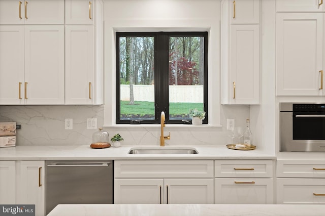 kitchen featuring backsplash, light stone countertops, appliances with stainless steel finishes, white cabinets, and a sink