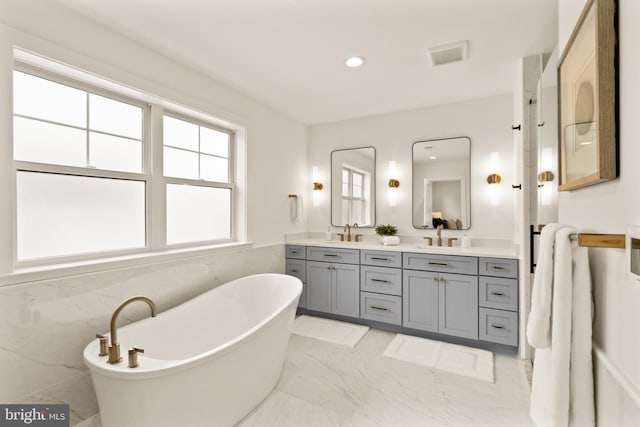 bathroom featuring visible vents, marble finish floor, a sink, double vanity, and a soaking tub